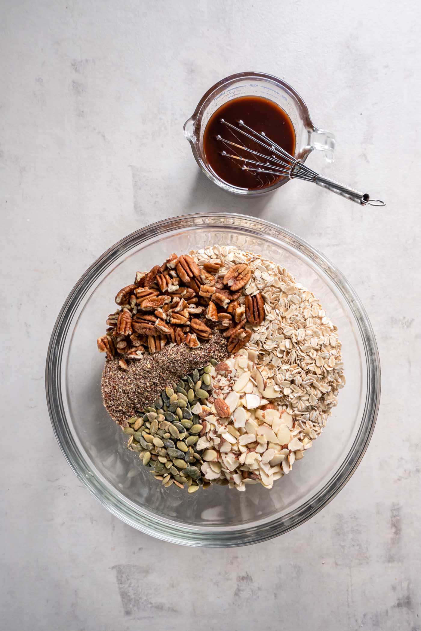 The BEST homemade granola recipe! This granola is easy to make with pantry ingredients, healthy and so much better than store bought! Oats, sliced almonds, pepitas, pecans and flaxseed in mixing bowl.